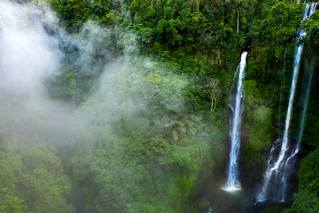 Aerial over Sekumpul waterfall surrounded by dense rainforest and mountains shrouded in mist at sunrise, Bali, Indonesia