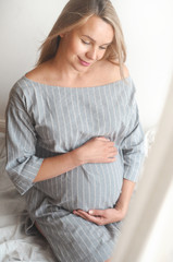 Happy pregnant woman sit on a bed at home and looking to the camera