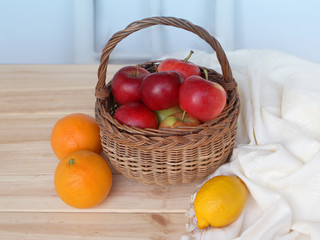 Wicker basket with fresh red apples stands on a light wooden background, on which lies a white...