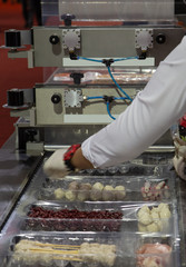 Industrial food worker put food in plastic tray for package sealing in machine
