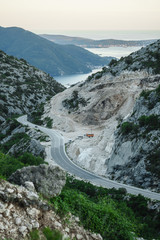The winding road leads through the mountains past the mining of granite. A beautiful view of the sunset sky mountains and the sea is visible in the distance