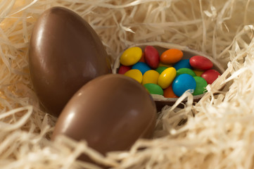 Easter. Chocolate eggs with multicolored candies lie in a nest on a wooden white table.