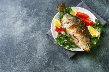 Baked carp fish with vegetables and spices on a plate on a dark table with a copy of space.