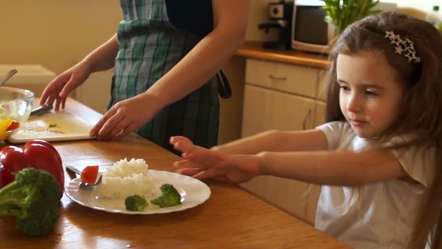 Little beautiful girl refuses to eat while sitting at the table in the kitchen. Children's whims