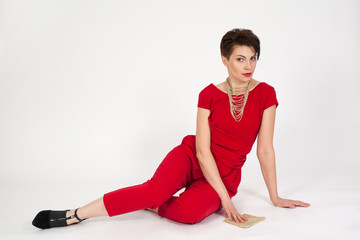 The young beautiful woman in in red dress on a white background looks into the camera.