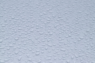 View of the big raindrops on the roof of a light blue car