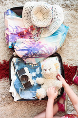 Suitcase with packed summer clothes, a camera, a hat and sunglasses