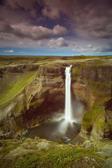 The Haifoss Waterfall with golden clouds in the sky. The flowing water is captured by a long...