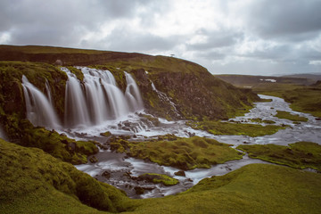 The Bláfjallakvísl Waterfall with golden clouds in the sky. The flowing water is captured by a long exposure. Amazing blue color of water from the glacier. Natural and colorful environment...