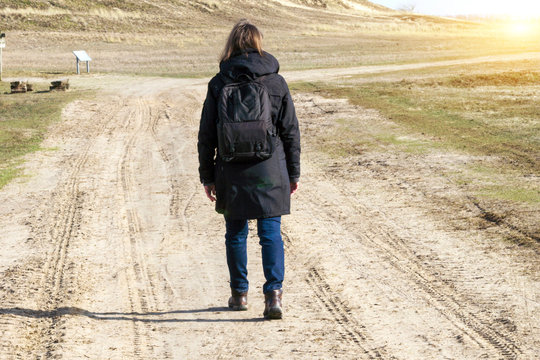 Europäische Frau in einer schwarzen Jacke hebt die Arme auf leerer Straße in Richtung zum Sonnenuntergang an