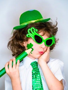Funny St Patricks day stunning little boy wearing a green hat. Self-Expression. Young boy drawing on himself a shamrock with a large green pencil.light background.
