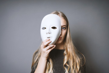 teen girl hiding her face behind mask - identity or personality concept - obrazy, fototapety, plakaty