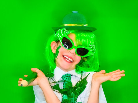Funny St Patricks day stunning little boy wearing a green hat, carnival glasses and a tie. Cute child posing with a big green pencil in his hands