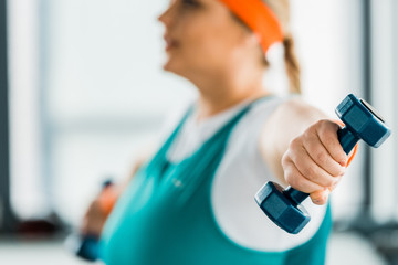 selective focus of dumbbell in hand of overweight woman