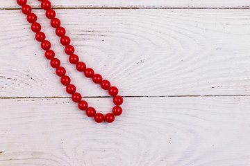 Red beads necklace on white wooden background. Top view