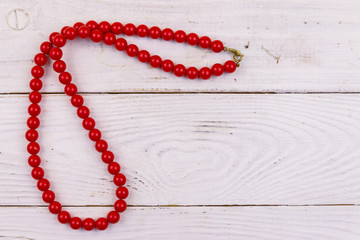 Red beads necklace on white wooden background. Top view