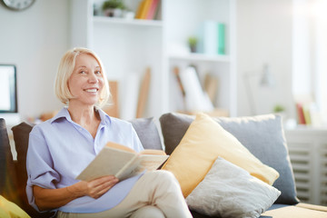 Obraz premium Portrait of contemporary adult woman smiling happily sitting on sofa at home and looking at camera, copy space