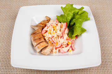 Corn and rice salad with chicken fillet on a white square plate.