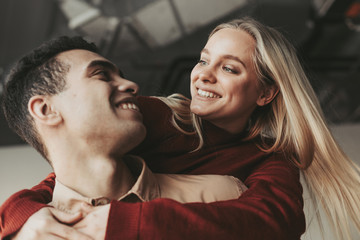 Cheerful nice young international couple hug and look at each other. They smile. Blonde woman and latino man looks happy