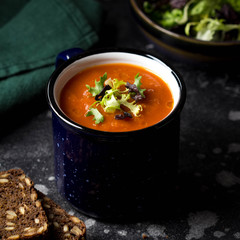 Orange vegetable cream soup in mug (tomato, carrot, lentil, pumpkin), delicious hot homemade lunch in cup. Dark background