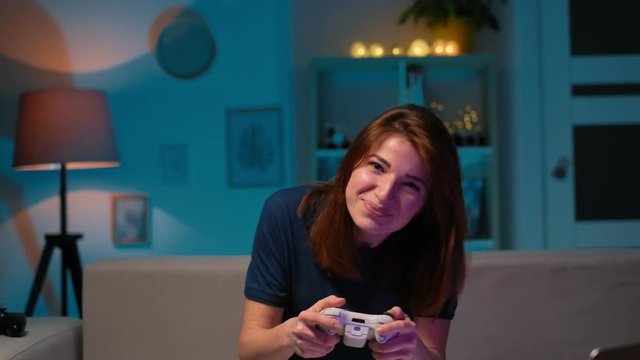 Determined girl playing a video game at living room at night. Excited gamer woman sitting on a couch, playing and winning in video games on a console, using a wireless controller.