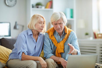 Obraz premium Portrait of contemporary adult couple looking at computer screen and frowning, copy space