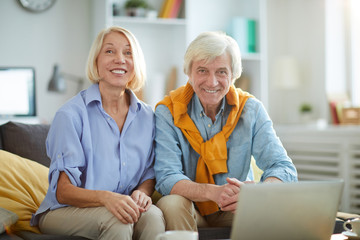 Obraz premium Portrait of contemporary senior couple sitting on sofa at home and looking at camera, copy space