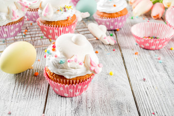 Easter kids party treat. Festive Easter food. Homemade cupcakes with cream and marshmallow cute bunny rabbits with paws. On a white wooden table, top view copy space