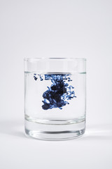 Water contamination concept. Dark substance dissolving with clean water in a glass in white background