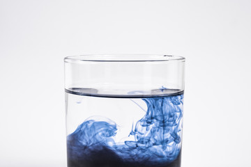 Water contamination concept. Dark substance dissolving with clean water in a glass in white background, close-up view