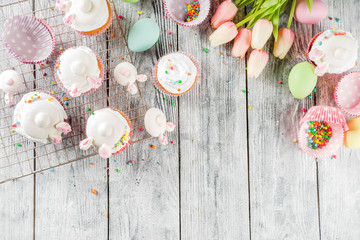 Easter kids party treat. Festive Easter food. Homemade cupcakes with cream and marshmallow cute bunny rabbits with paws. On a white wooden table, top view copy space