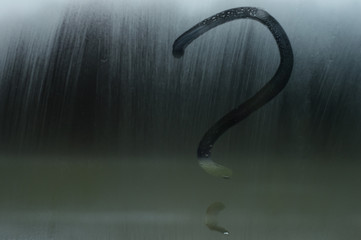 A question mark is drawn with a finger on a misted window. The question is painted on glass or on a mirror.