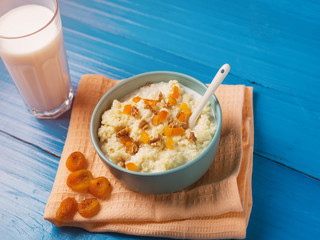 Millet porridge with milk on a wooden blue background with walnuts and dried fruits