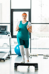 Fototapeta premium overweight girl exercising on step platform near sport equipment