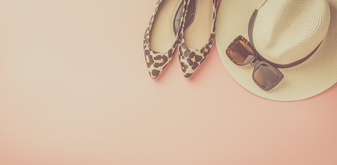 Straw hat, sunglasses and trendy leopard print shoes on pastel pink background, summer fashion concept. Top view, selective focus