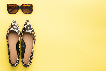 Sunglasses and trendy leopard print shoes on pastel yellow background, summer fashion concept. Top view, selective focus