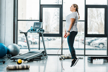 attractive plus size woman exercising with jumping rope in gym