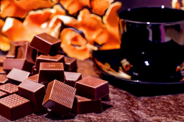 Chocolates, cup of coffee and tangerines. Selective focus. Blurred background. Dark tones. Autumn motives. Vintage.