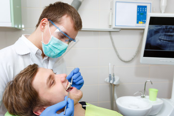Closeup portrait of student male in dentist chair having teeth examined by young dentist in dental office with x-ray on background. Dental care for people. Dentistry, medicine and health care concept