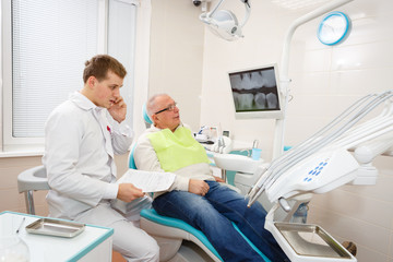 Senior man 70-75 years old on review of dentist, sitting in chair dental office. Focus on x-ray. Dental care for older people. Health care concept