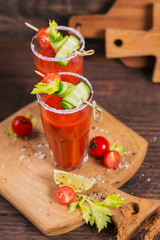 Two glasses of tomato juice decorated with fresh tomatoes, cucumber and leaves on a wooden background