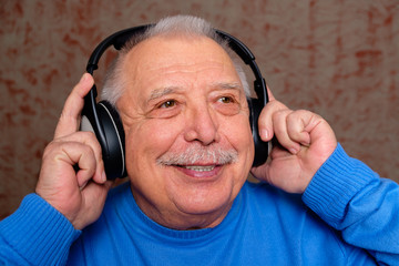 Close Up portrait senior old man with mustache in casual wear and headphones is listening to music and smiling, on gray background