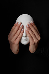 Girl's hands close eyes of plaster mask face on a black background. See no evil. Concept three wise monkeys.