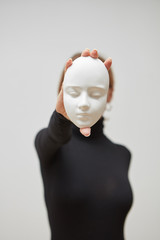 Plaster mask in the hand of young female instead face on a white background, place for text. Concept The masks we wear.