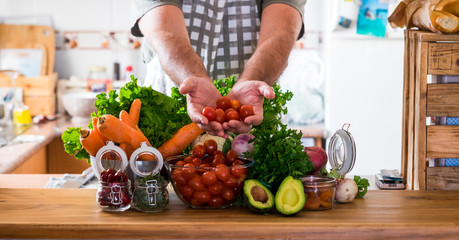 Vegetarian and healthy food lifestyle at home concept - table in the kitchen full of mixed coloured vegetables and man hands showing you the freshness - background and energy infredients to cook