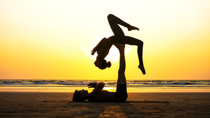 Silhouette of fit sporty couple practicing acrobatic yoga with partner together on the beach in...