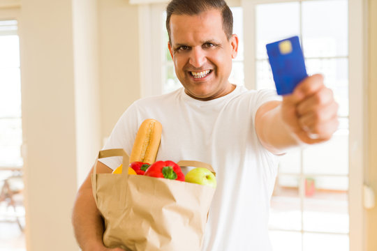 Middle age man holding groceries bag and showing credit card
