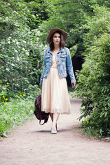Young woman in denim jacket and hat walking in park outdoors