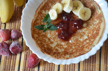 freshly fried homemade french crepes on a plate with strawberries, banana slices and fresh cream, horizontal view from above, close-up