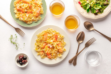 An overhead photo of a plate of salmon pasta, Farfalle with smoked salmon and cream sauce, shot from the top with wine and salad